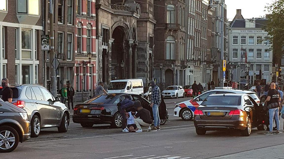 Khurshid kneels on the ground surrounded by Dutch police and police cars, as he is arrested on a busy street in Amsterdam.