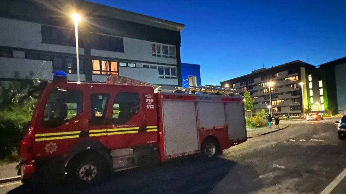 A fire engine outside the flats, with a street light and other premises behind