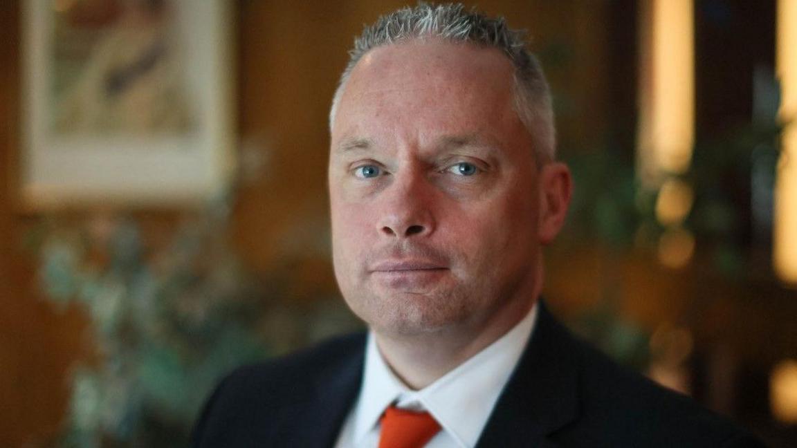 A man with short grey hair and wearing a suit with a red tie