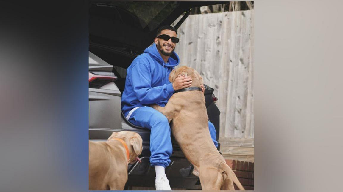 Said Benrahma with his two dogs at the back of his car. One is reaching up to see him and the other one is standing nearby.