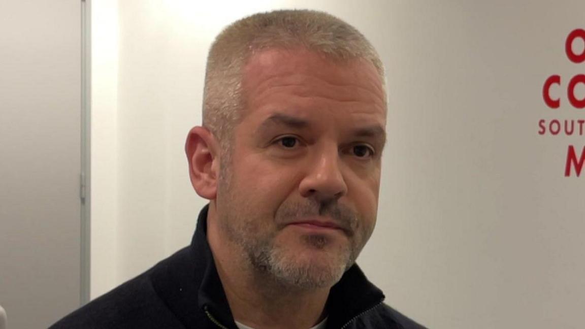 A man with very short greying hair and a salt and pepper beard.