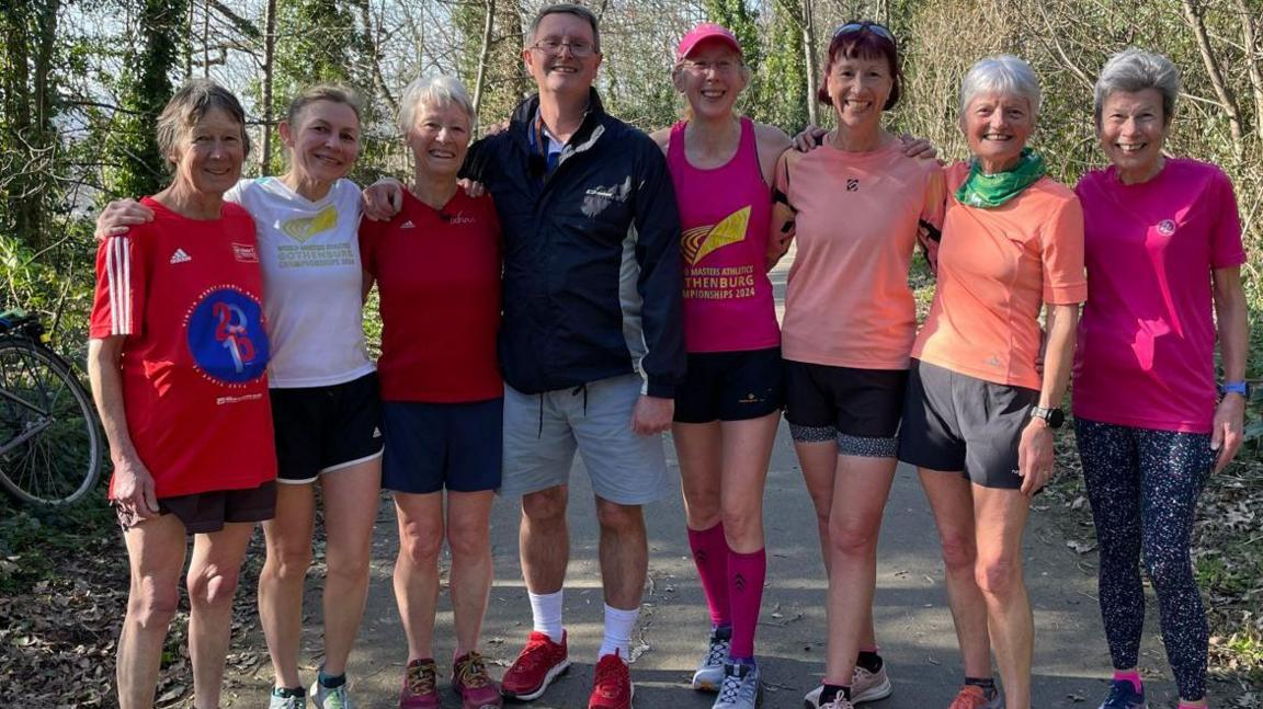 Group of women runners including John Rothwell plus their male running coach  John Rothwell at Clay Wood in Sheffield. They're all smiling at the camera having finished their running training session.