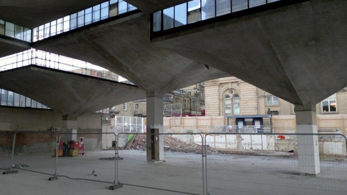 Grey concrete arches on top of pillars, with windows at the top as well. There are metal fences as bricks and work has started on the project.