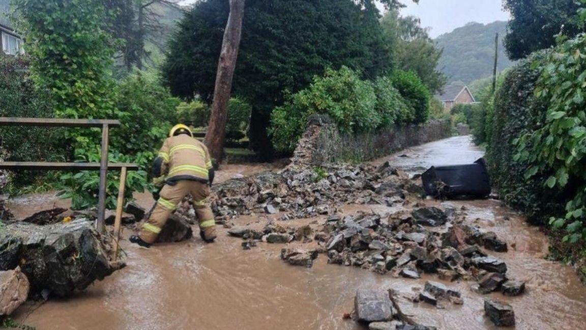 A firefighter clearing a flooded road with rocks strewn along it