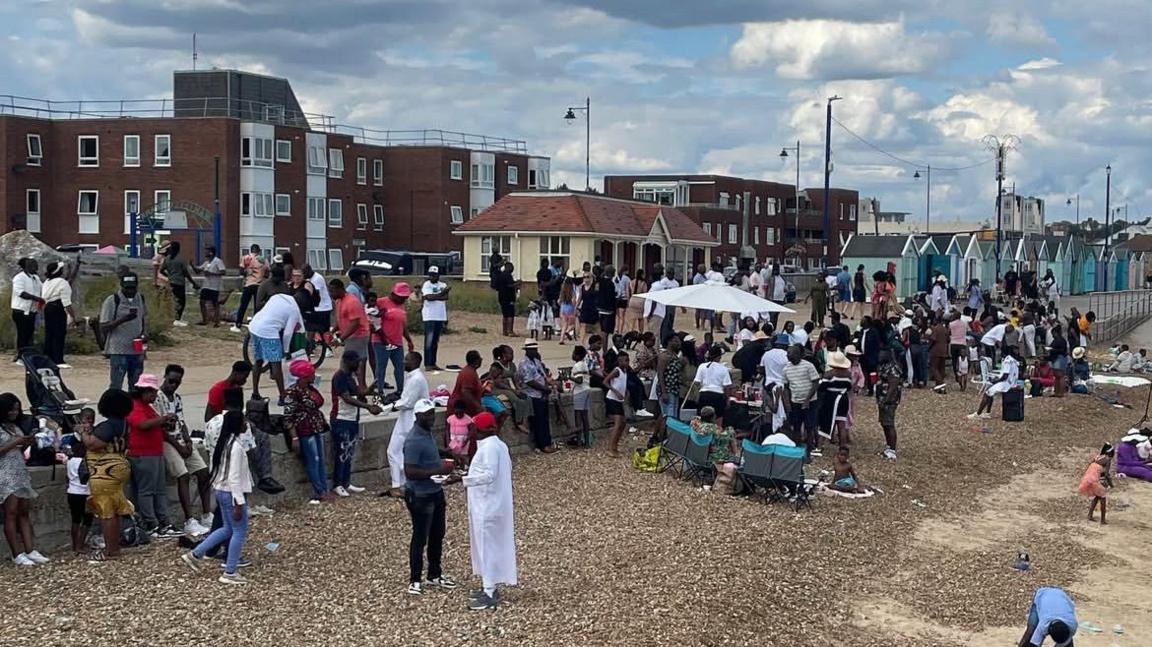 Tens of people gather on a beach during an event.