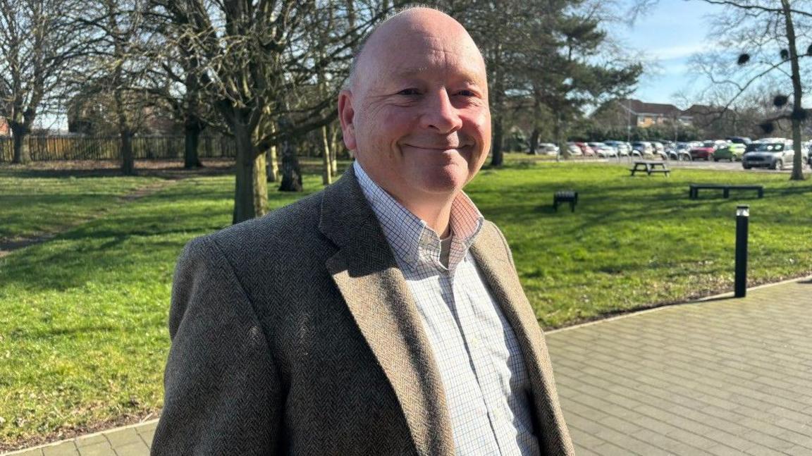 Councillor Travis Hesketh pictured outside the council offices in Horncastle. He is wearing a shirt and suit jacket and is looking towards the camera.