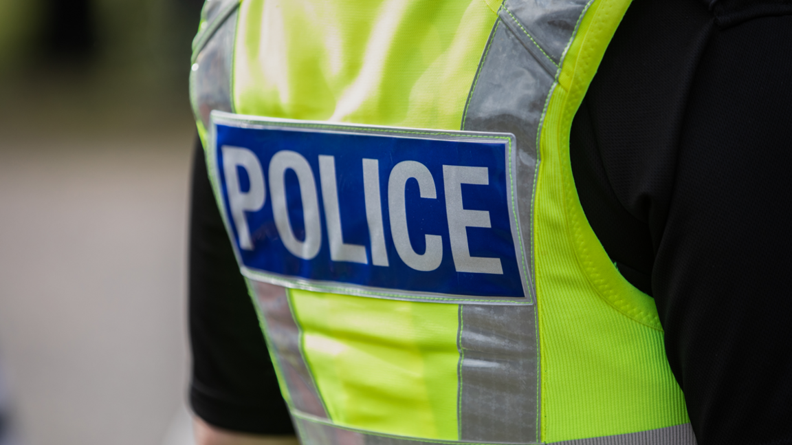 The back of a police officer's uniform, showing a green hi-vis jacket with 'police' written on it