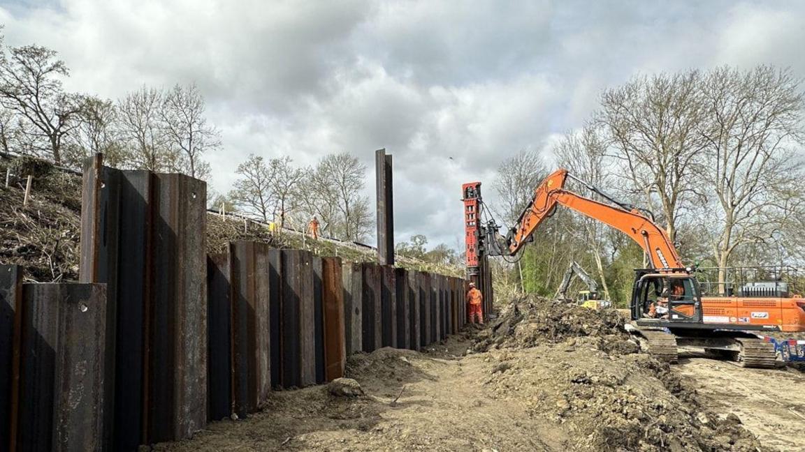 A large orange digger working to dig dirt. There are trees in the background.