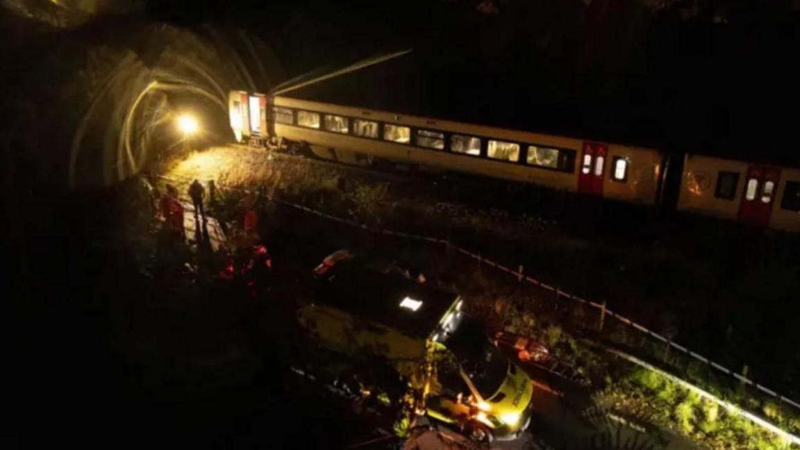 The train carriage on the track at night after the crash with emergency vehicle by the road