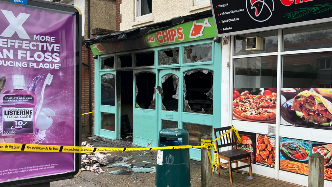 The badly-damaged front of a fish and ship shop in Norwich. The windows are smashed and a yellow piece of tape cordons off the scene.  