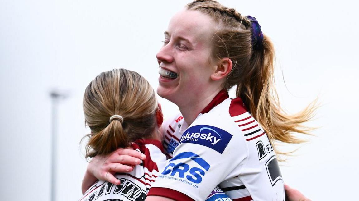 Ellise Derbyshire hugs Ruby Hunter as she celebrates scoring for Wigan Warriors Women.