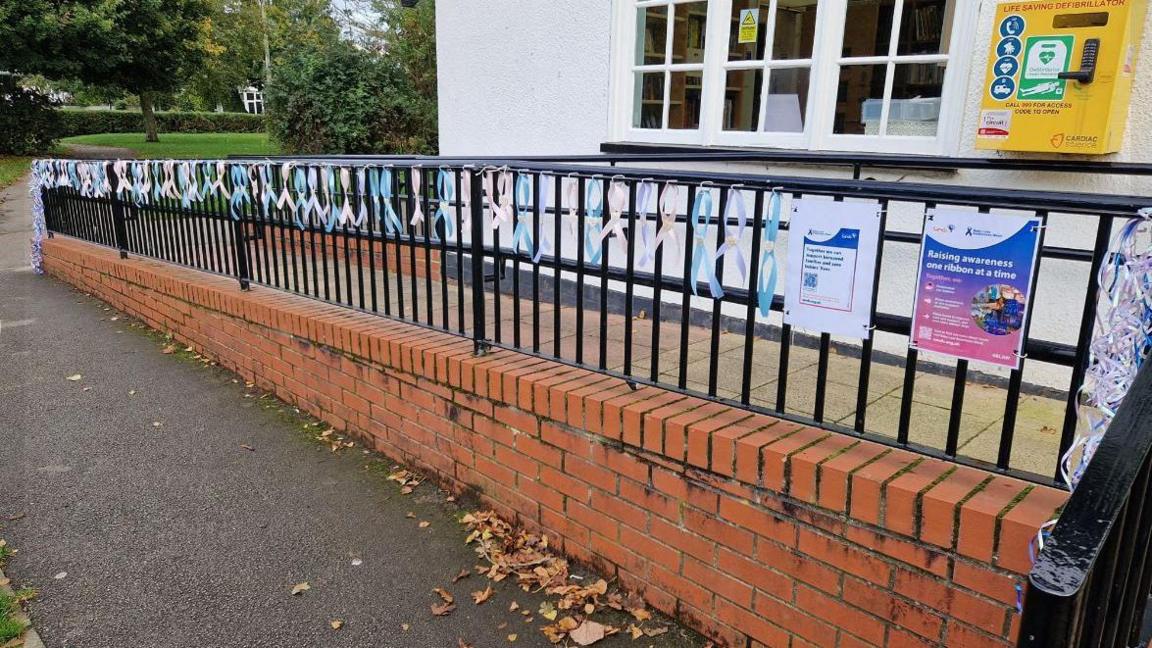 Several pastel-coloured ribbons with wooden hearts in the middle dotted along a railing at a park's library