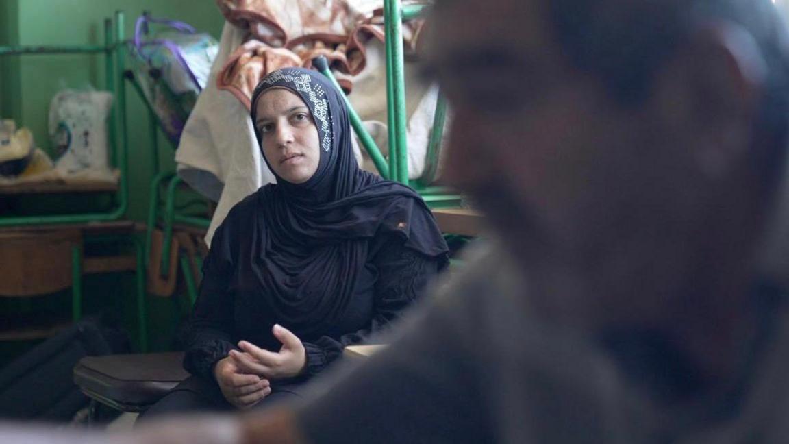 A young woman sits with her hands on her lap, looking pensive