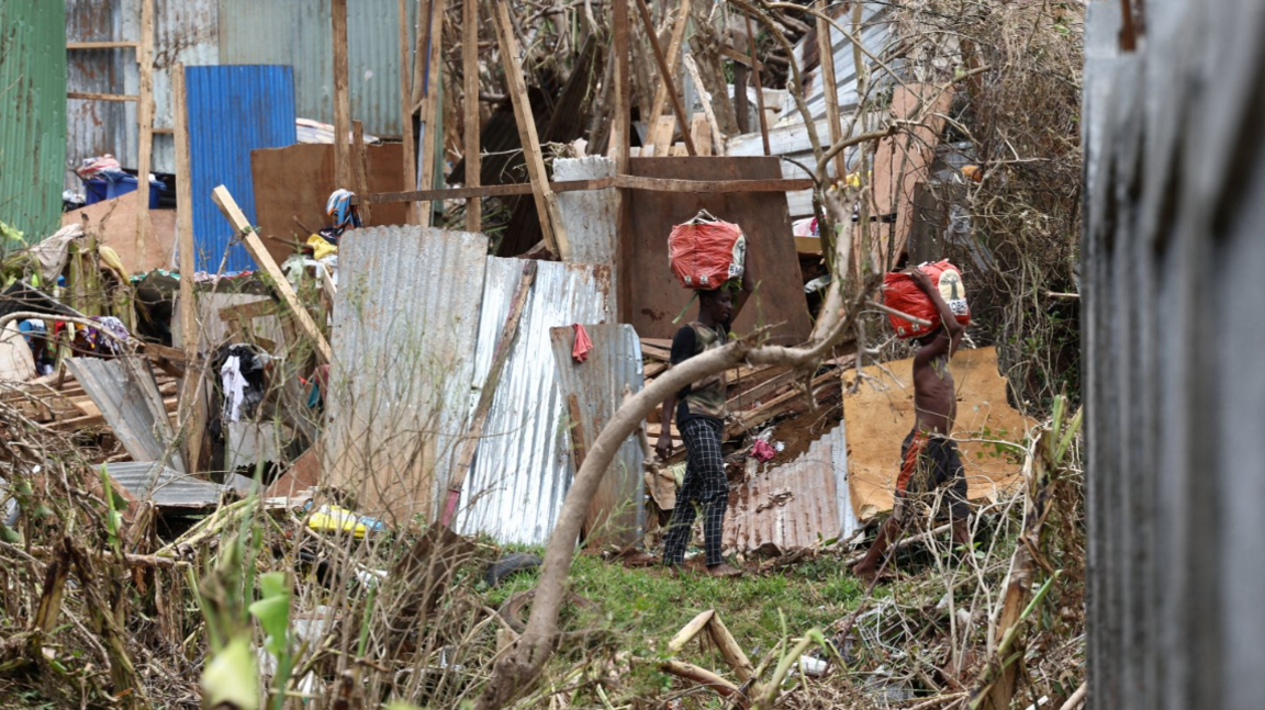 Two people are seen carrying bags on their heads amid strewn tin panels and timber from destroyed shacks