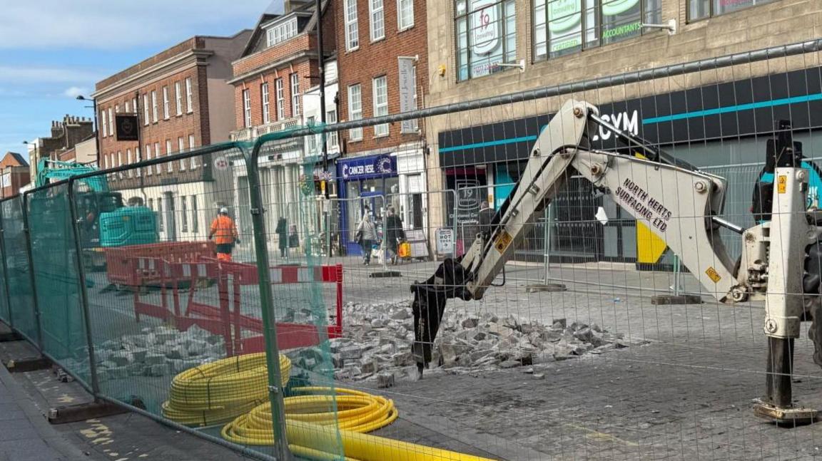 Cobbles being removed from a road by heavy plant machinery.