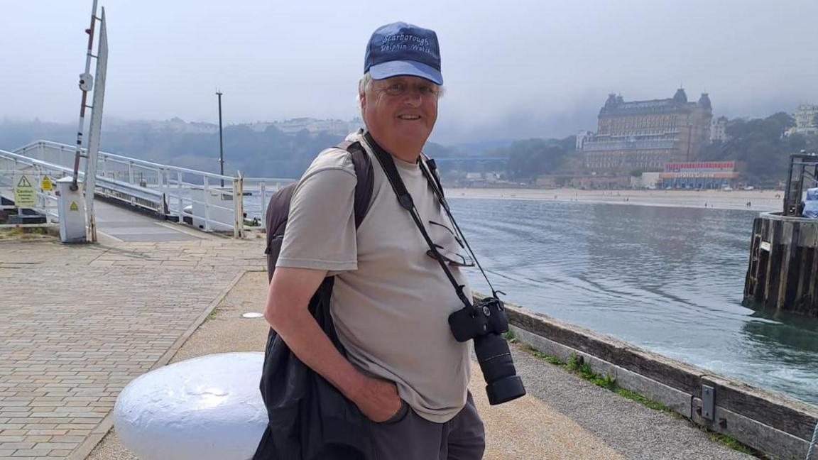A man in a blue cap and brown t-shirt standing by the pier at Scarborough.