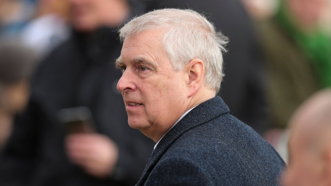 Prince Andrew standing outside in an overcoat, pictured from the side with the background blurred. He has white hair and a neutral expression. 