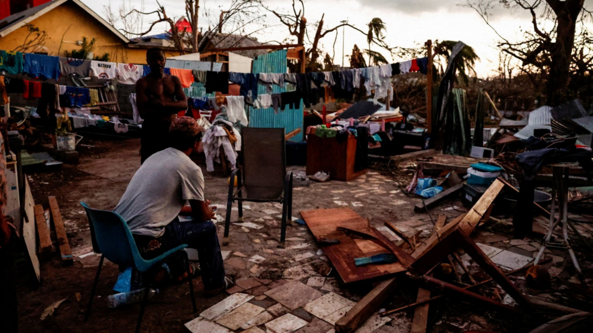 A man sits on a chair in the backyard of a damaged house in the aftermath of Cyclone Chido as clouds are seen overhead