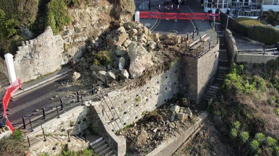 A rockfall has spilled down a cliff and covered a coastal road.