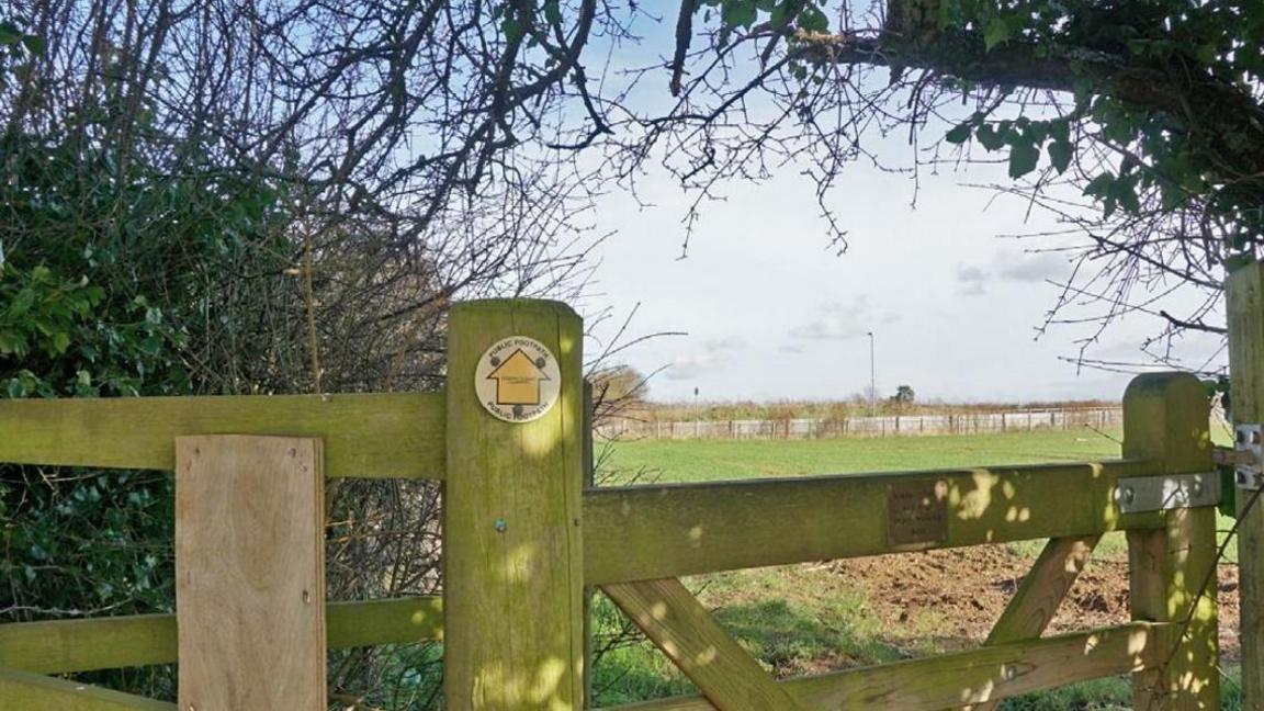 A wooden public footpath gate leading to the field where the 187 homes will be built in the background