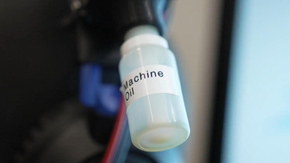 A clear plastic bottles attached to a machine with a label on it reading "Machine Oil". 