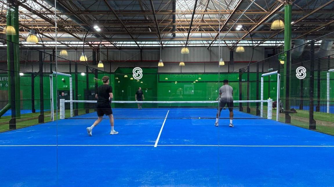 Four people playing padel on a blue court.