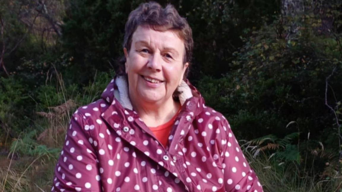 A woman wearing a polka dot jacket sits outside on a log