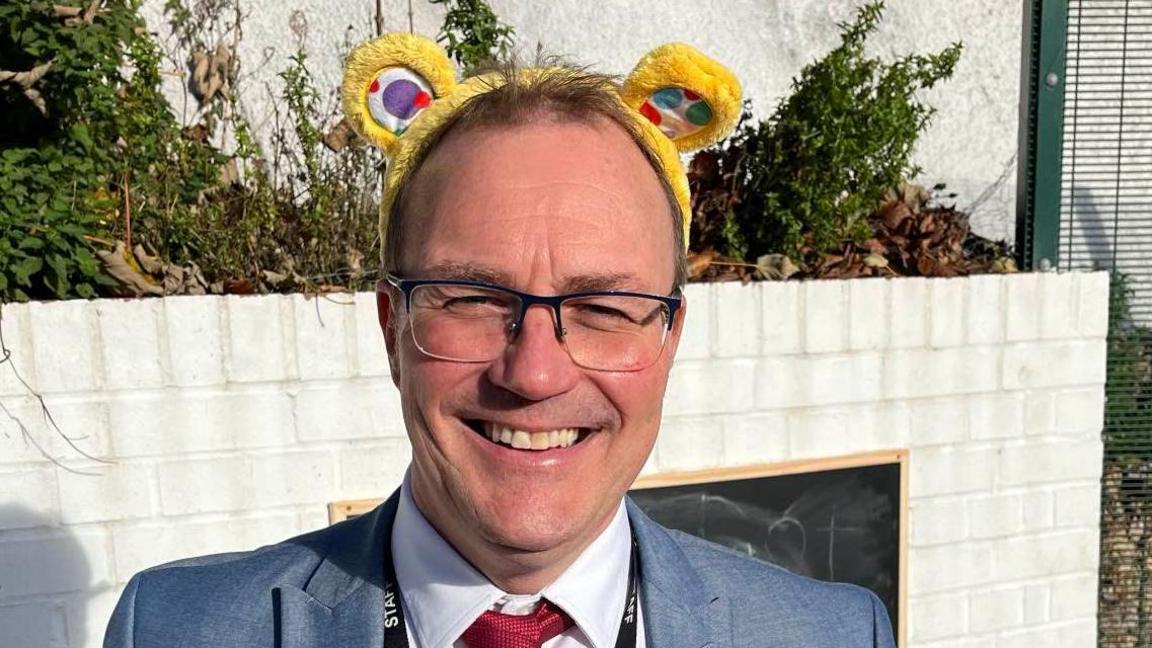 David Whitehead, CEO of Our Community Multi Academy Trust, stands in Borden Primary School playground wearing Pudsey ears on his head