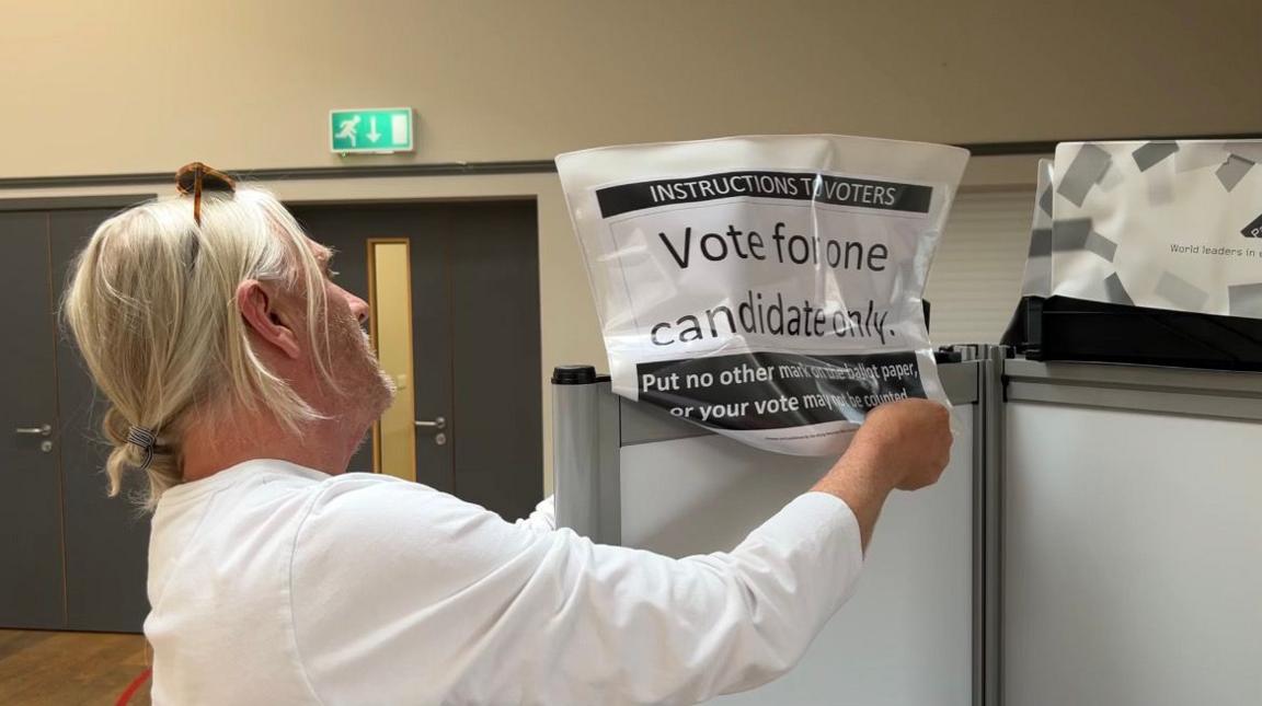 Man in white top setting up a polling booth