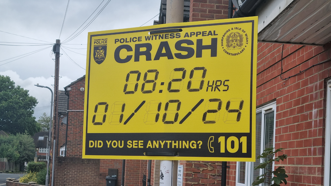 A yellow sign notifying people of the crash, with Thames Valley Police and Hampshire and Isle of Wight Constabulary insignia, and writing that says: "Police witness appeal: crash. 08:20 hrs, 01/10/24. Did you see anything? [Call] 101."