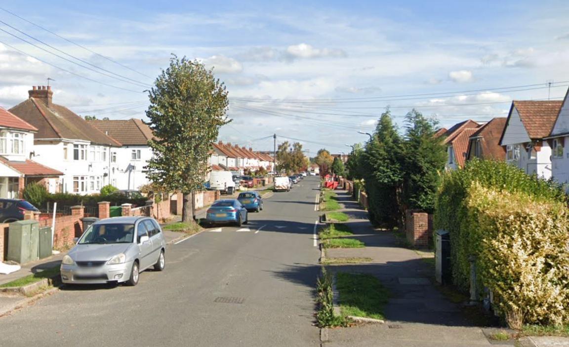 A Google street view screenshot of a sunny street with semi-detached houses on each side and cars parked on the roadside.