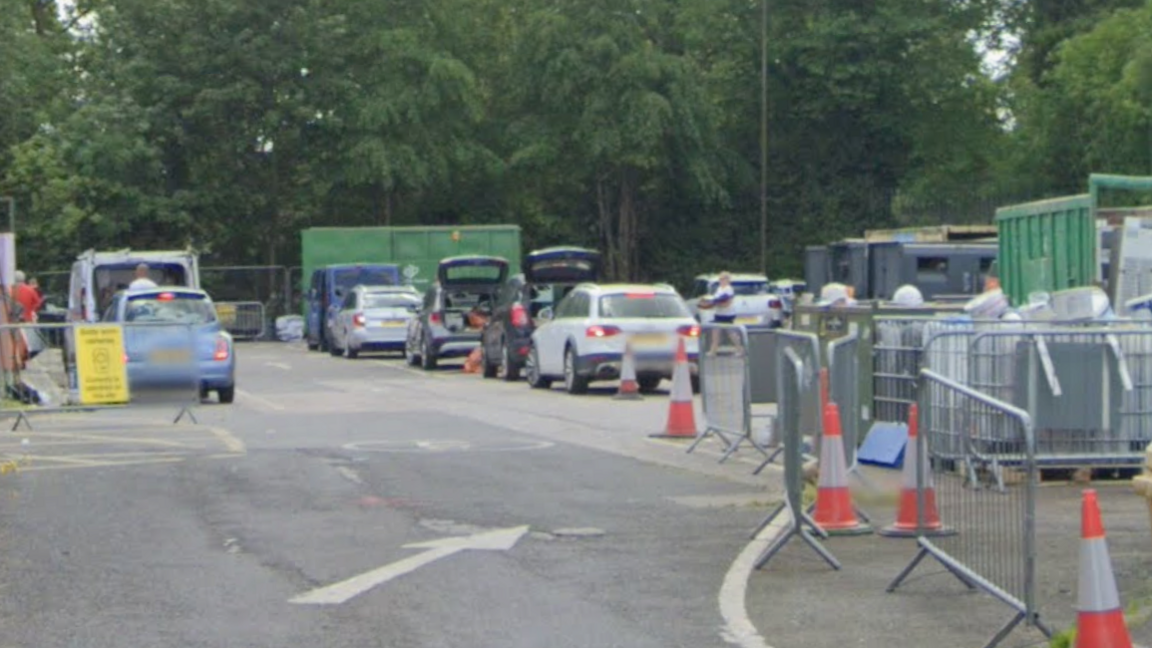 A number of cars parked with cones and fencing to the right of the image