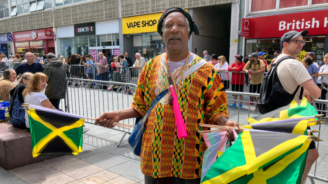 A man holding Jamaican flags with lining the streets to celebrate Leicester's 40th Caribbean Carnival in 2025.