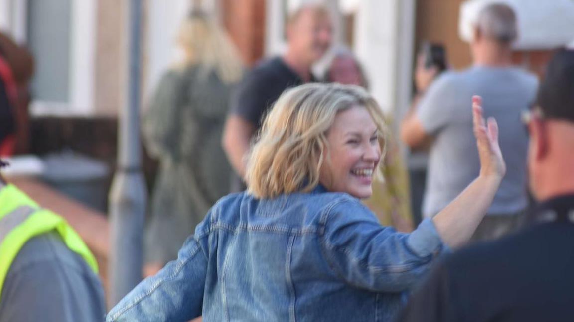 Joanna Page wearing a denim jacket and turning towards the camera with a wave