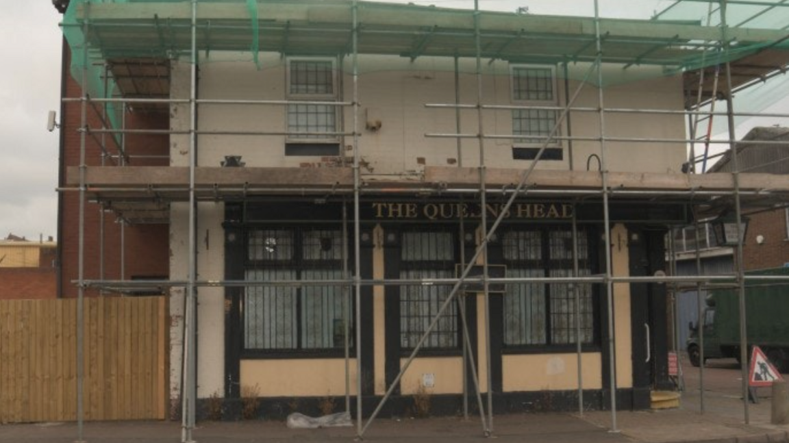 Scaffolding surrounds the Queen's Head pub which is on the corner of a street.