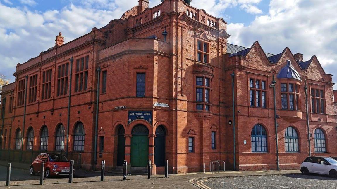 An exterior shot of Salford Lads Club. It is a large, two-storey red brick Victorian building with a green door.