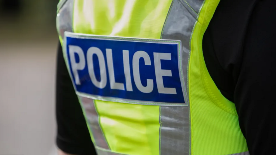 the back of a British police vest. It is bright yellow with the word POLICE in bold white lettering against a blue backdrop