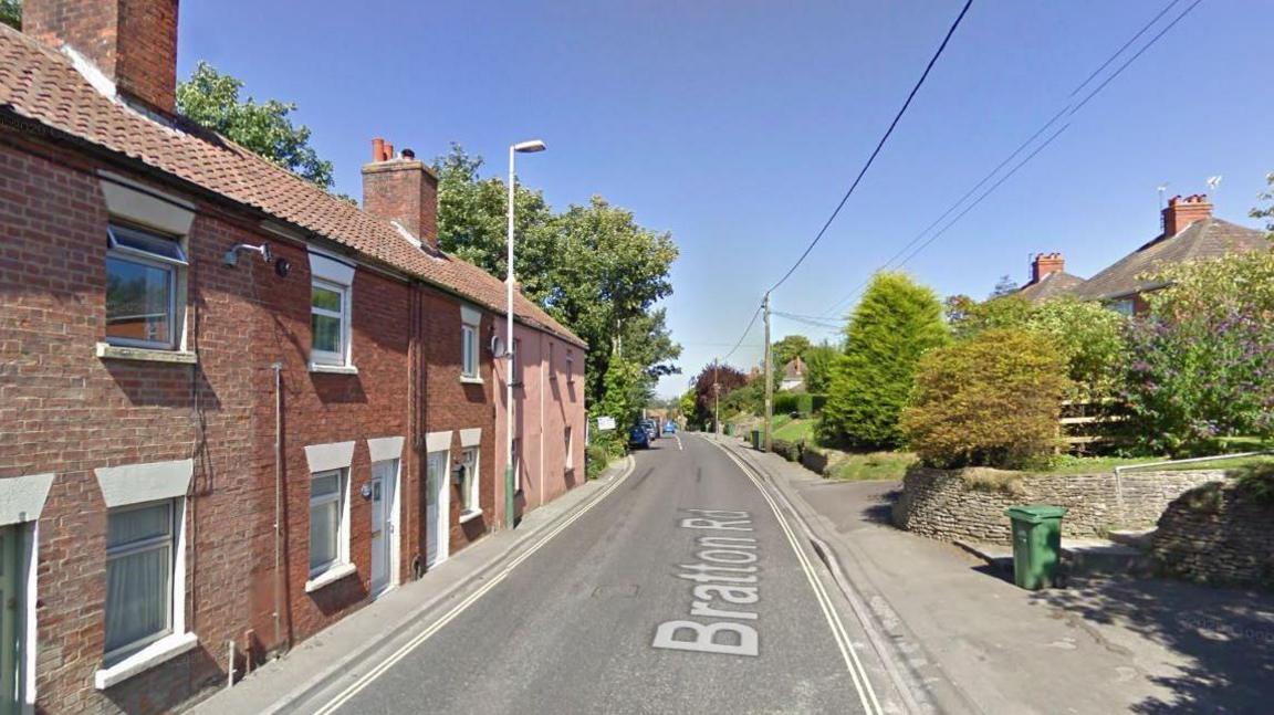 A google maps shot of a section of Bratton Road when empty - it has terraced house son the left, with doors that open up right onto the pavement, which itself is very narrow. On the right, housing also, but with large front gardens.