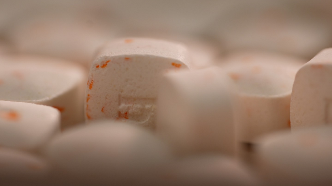 Close up photo of finasteride pills, which are white and speckled with orange