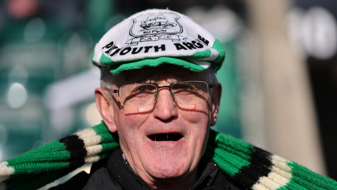 A picture of an man with glasses, grey hair and wearing a green scarf.