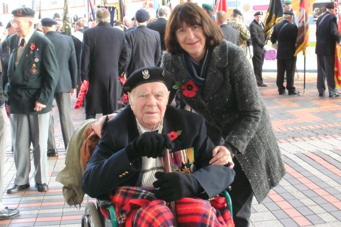 Cpl Andrzej Gasior wearing a Polish Army beret and medals sits in a wheelchair with a blanket over his knees at a Remembrance Day service in Birmingham with daughter Sue Butler by his side