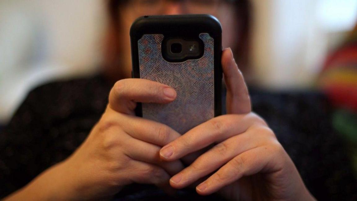 A woman, who is out of vision, is holding a mobile phone with a glittery protective case in front of her face.