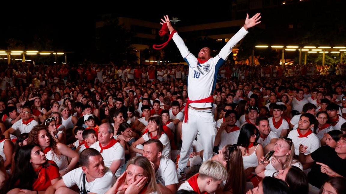 England fan stands up to celebrate while surrounded by Spain fans