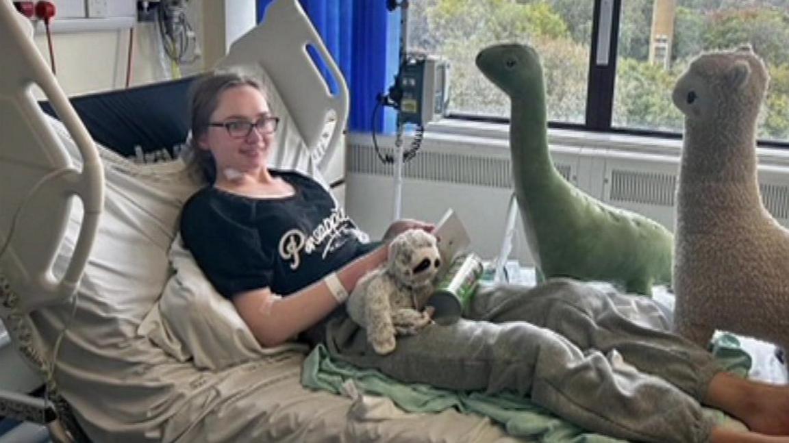 Eliana sits in a hospital bed with cuddly toys