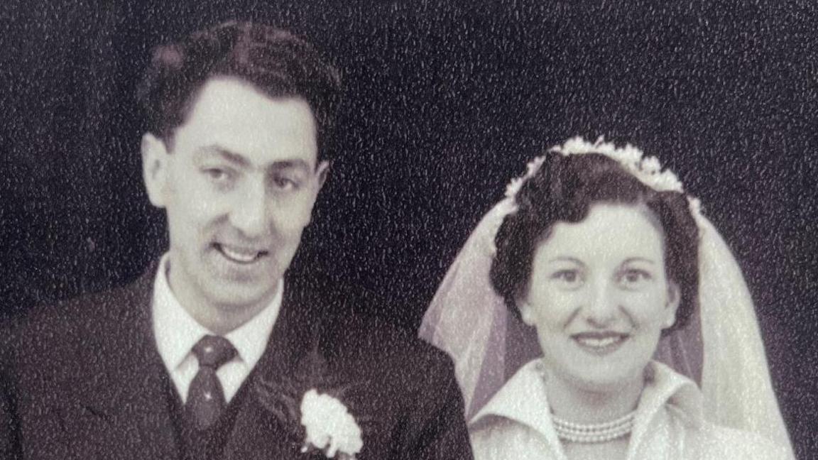 A black and white image of Ron and Nancy Ashpool on their wedding day. Mr Ashpool is wearing a suit and Mrs Ashpool a white wedding dress.