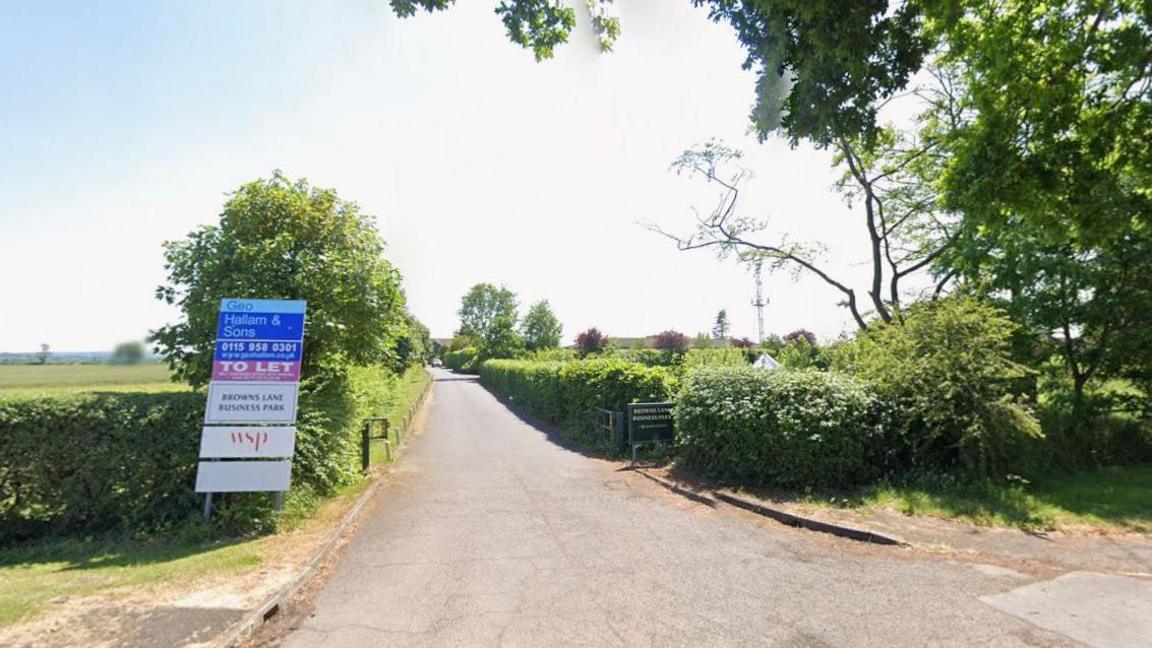 A single track road with hedges either side, with two signs marked Browns Lane Business Park alongside a To Let sign