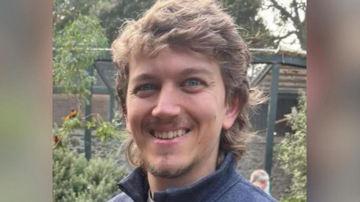 Dafydd Bayliss, who has long fair hair in a mullet style and short facial hair. He is smiling in the photo.