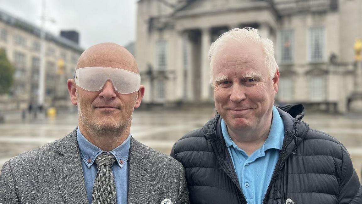 Two men stood outside Leeds Civic Hall. One is wearing specially adapted glasses to replicate what it's like to be partially sighted. 