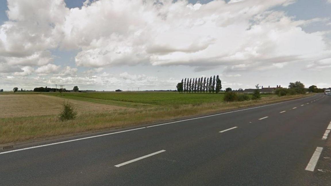 Part of the A47 between Thorney and Eye in Cambridgeshire. The surrounding landscape is flat and there are fields and trees in the background