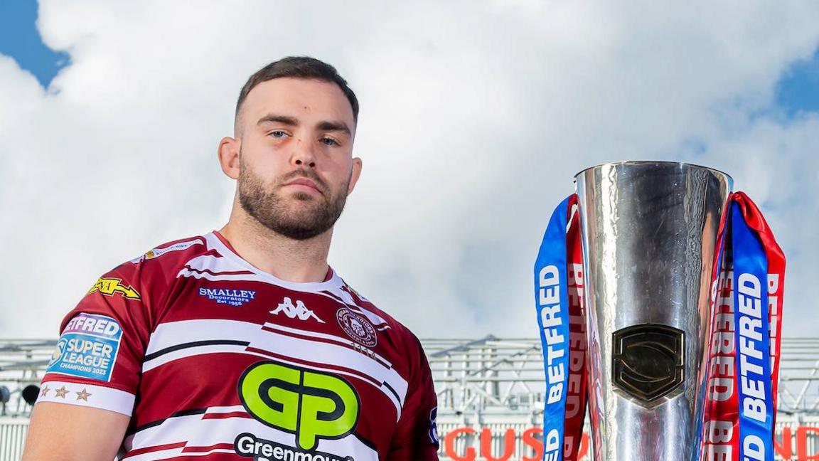 Wigan's Kaide Ellis stands with the Super League trophy